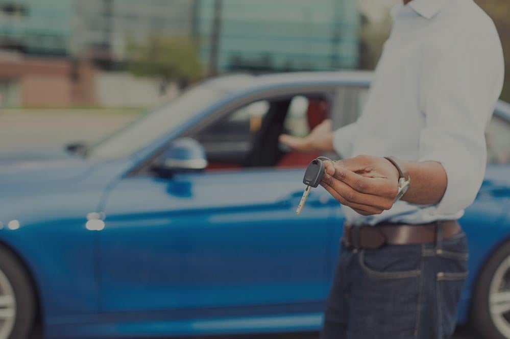 mann mit schlüssel vor blauem auto